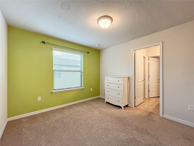 unfurnished bedroom featuring light carpet, a textured ceiling, and baseboards