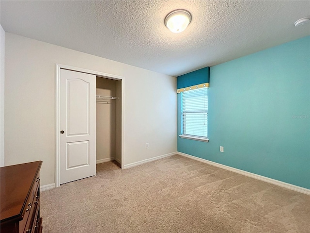 unfurnished bedroom featuring light carpet, a closet, a textured ceiling, and baseboards