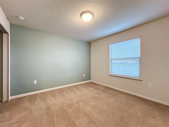 spare room featuring light carpet, baseboards, and a textured ceiling