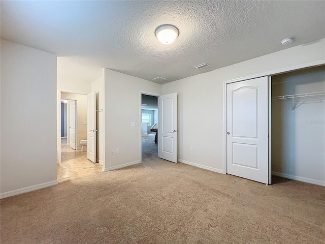 unfurnished bedroom with a closet, visible vents, light carpet, a textured ceiling, and baseboards