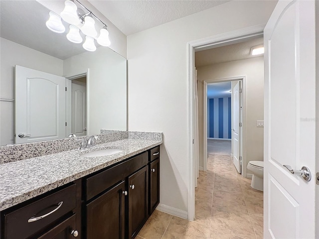 bathroom with baseboards, vanity, toilet, and a textured ceiling