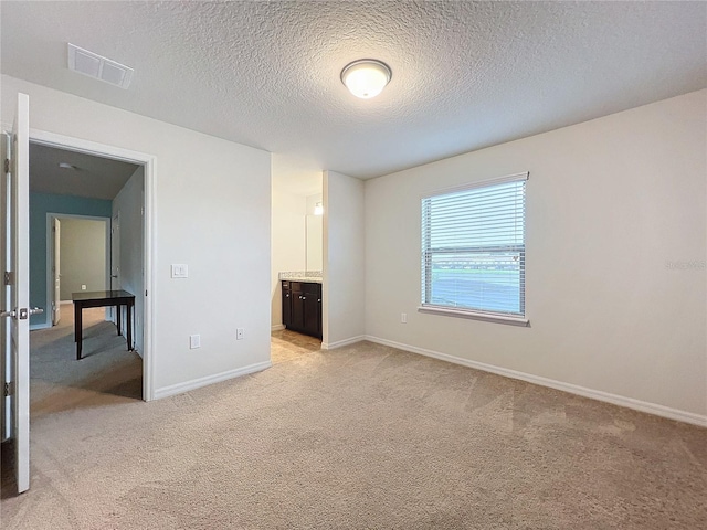 unfurnished bedroom featuring light carpet, baseboards, visible vents, connected bathroom, and a textured ceiling