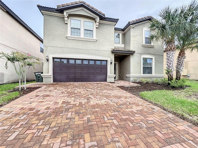 mediterranean / spanish-style home with a garage, a tile roof, decorative driveway, and stucco siding