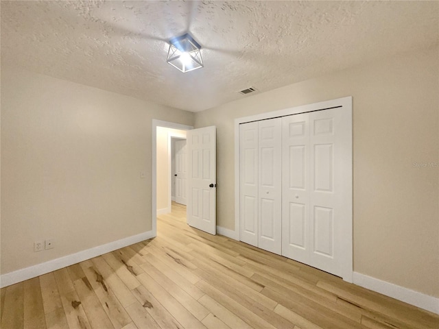 unfurnished bedroom featuring a closet, a textured ceiling, and light hardwood / wood-style flooring