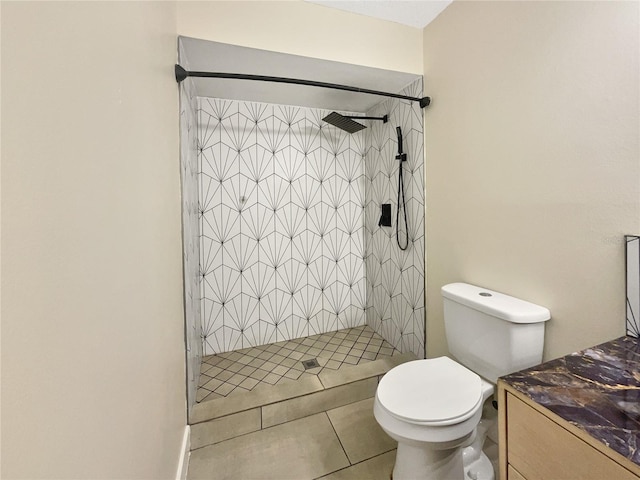 bathroom with tile patterned floors, vanity, tiled shower, and toilet