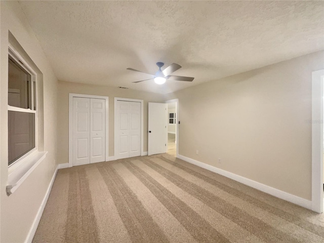 unfurnished bedroom with ceiling fan, multiple closets, a textured ceiling, and carpet floors