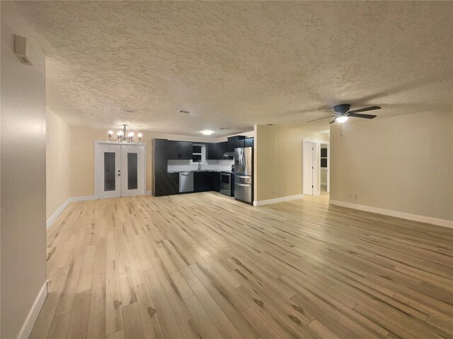 unfurnished living room featuring light hardwood / wood-style floors, french doors, sink, a textured ceiling, and ceiling fan with notable chandelier