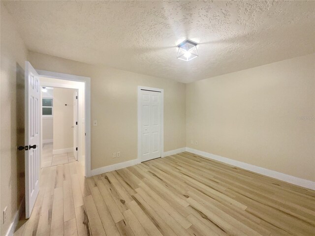 unfurnished bedroom featuring light hardwood / wood-style floors, a textured ceiling, and a closet