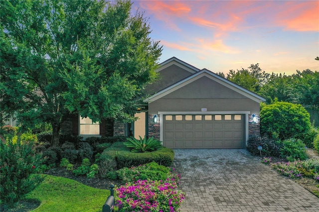 view of front of home featuring a garage, stone siding, decorative driveway, and stucco siding