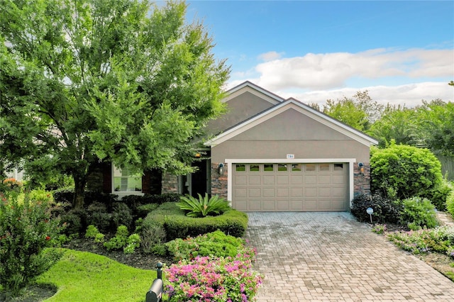 view of front of property featuring an attached garage, stone siding, decorative driveway, and stucco siding