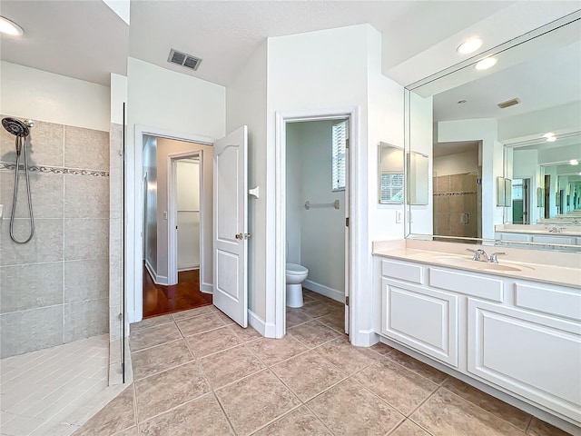 bathroom with tile patterned flooring, vanity, a tile shower, and toilet