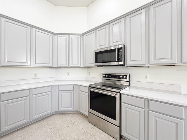 kitchen with stainless steel appliances, gray cabinetry, light tile patterned floors, and light stone counters