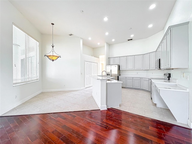 kitchen with an island with sink, appliances with stainless steel finishes, gray cabinetry, and light hardwood / wood-style flooring