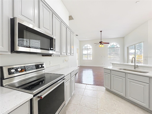 kitchen featuring light tile patterned flooring, sink, light stone counters, appliances with stainless steel finishes, and ceiling fan