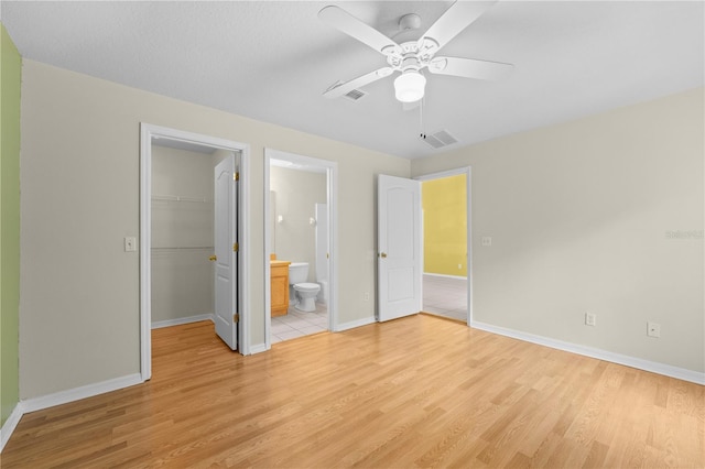 unfurnished bedroom featuring a walk in closet, light hardwood / wood-style floors, a closet, ceiling fan, and connected bathroom