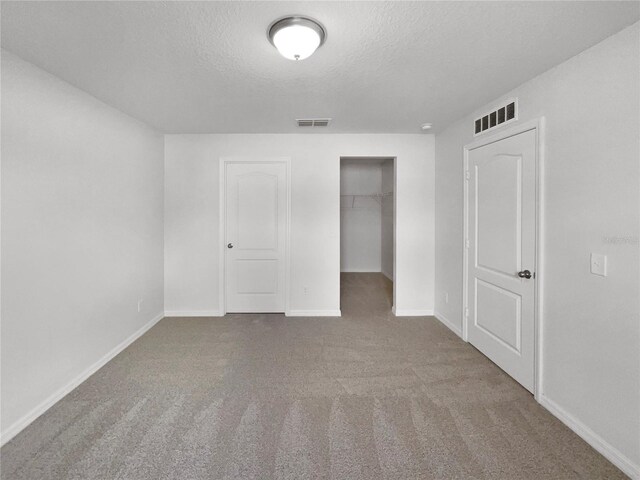 unfurnished bedroom with carpet, a closet, a textured ceiling, and a walk in closet