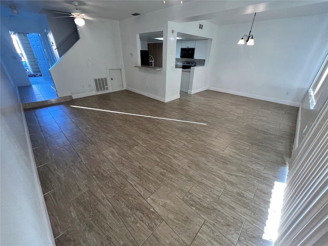 unfurnished living room with baseboards, visible vents, and ceiling fan with notable chandelier