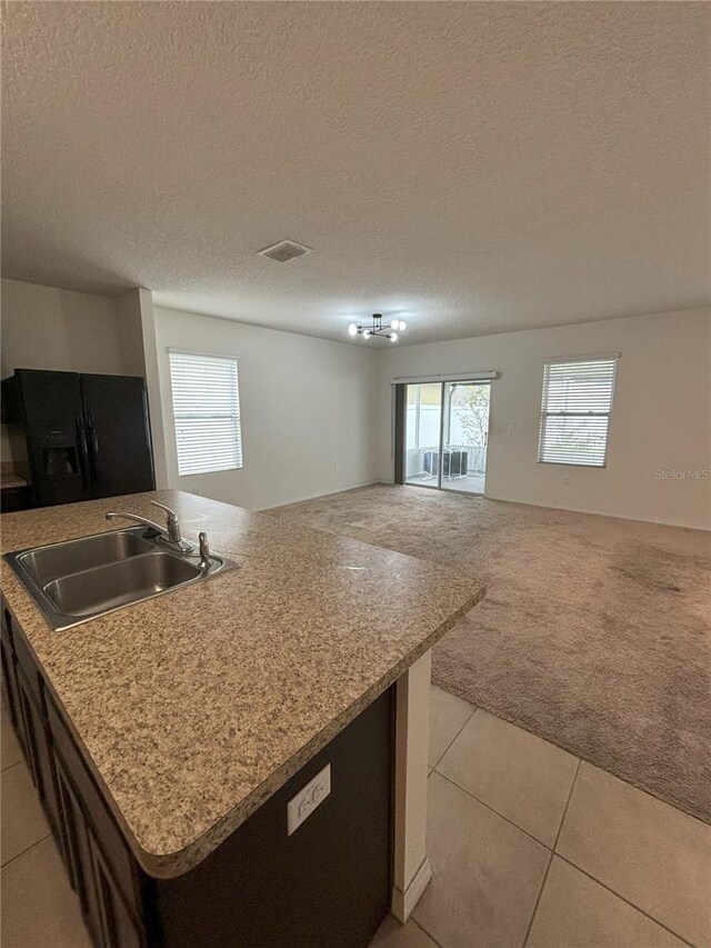 kitchen with a sink, black fridge, open floor plan, light colored carpet, and light tile patterned floors