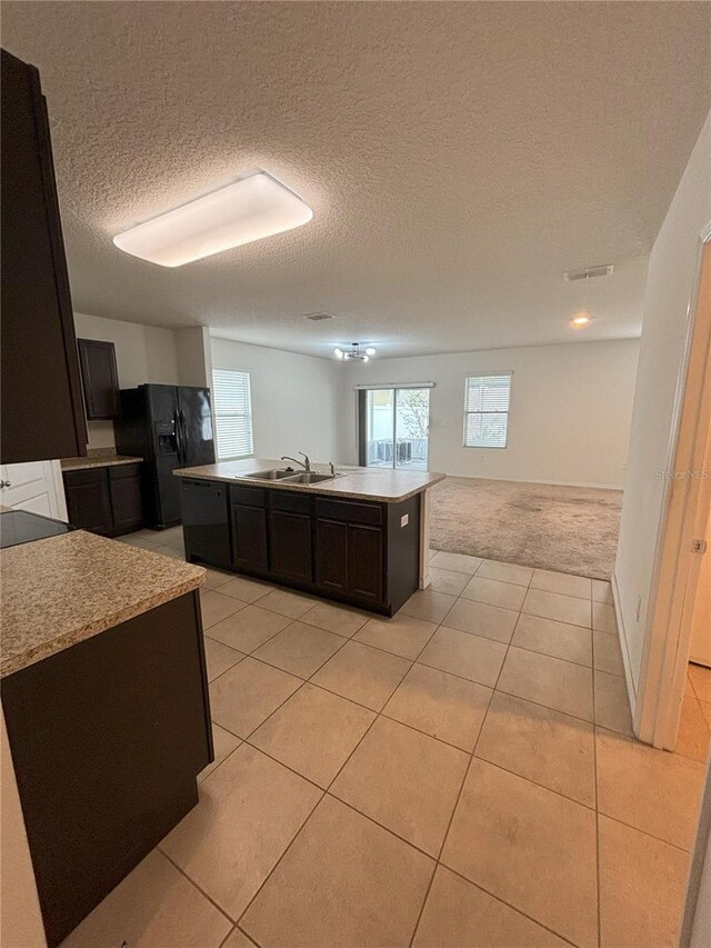 kitchen with plenty of natural light, an island with sink, a sink, open floor plan, and black fridge