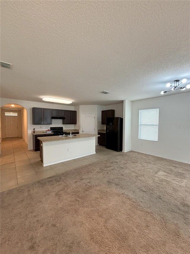 unfurnished living room with arched walkways, a textured ceiling, visible vents, and light carpet