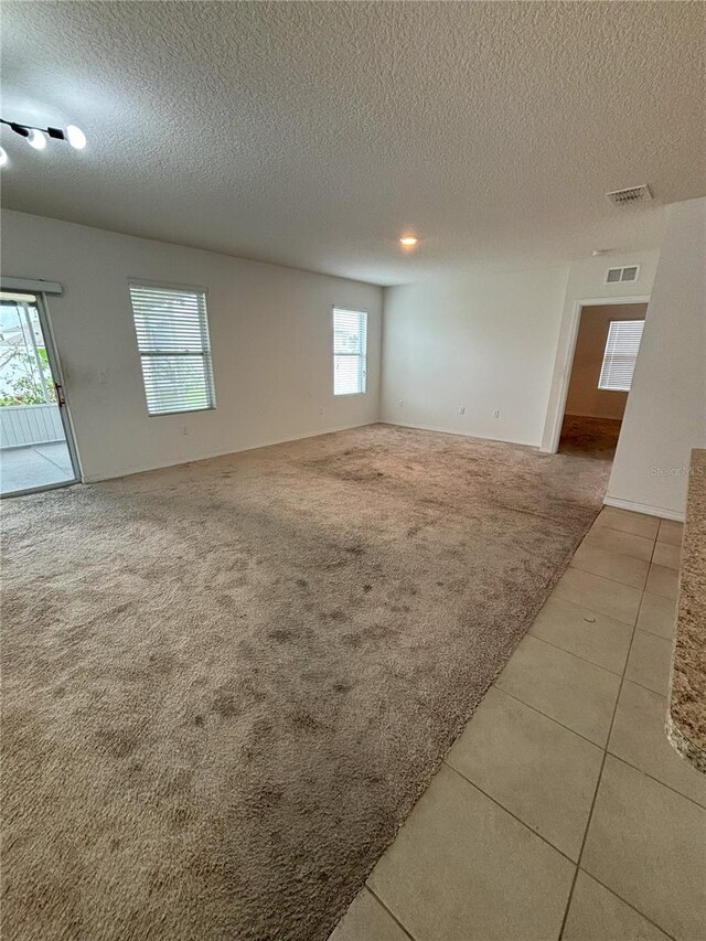 carpeted spare room with tile patterned floors, a textured ceiling, and visible vents