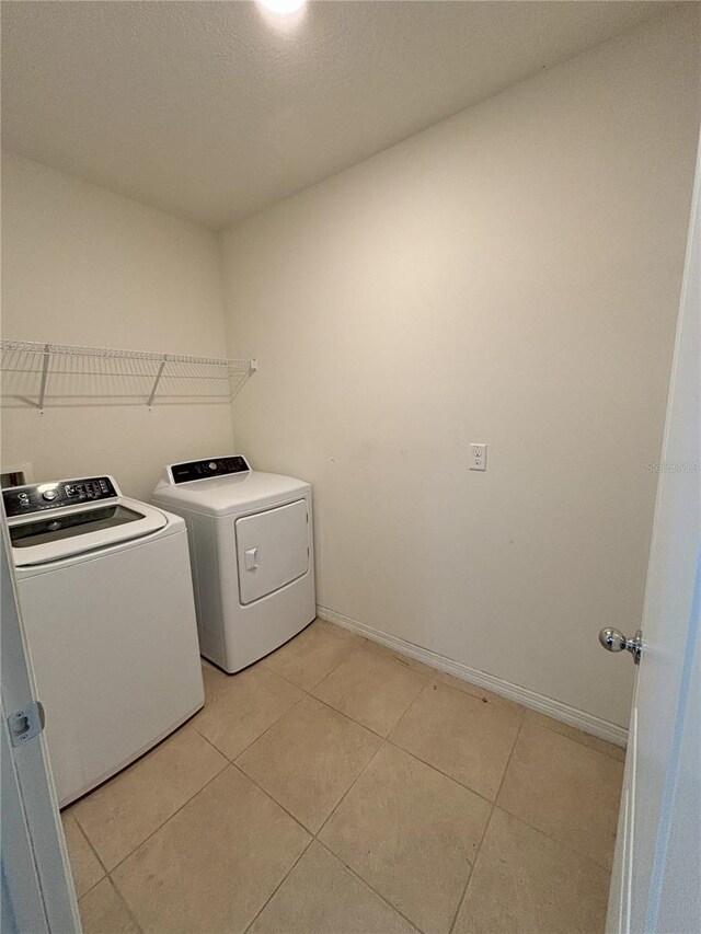 laundry area with washing machine and dryer, baseboards, laundry area, and light tile patterned floors