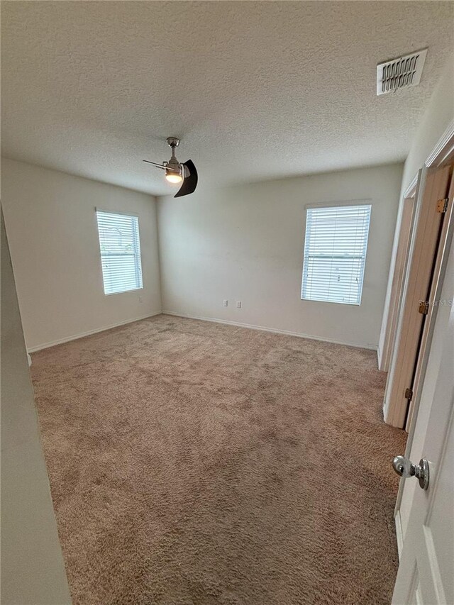 carpeted spare room with baseboards, a ceiling fan, visible vents, and a textured ceiling