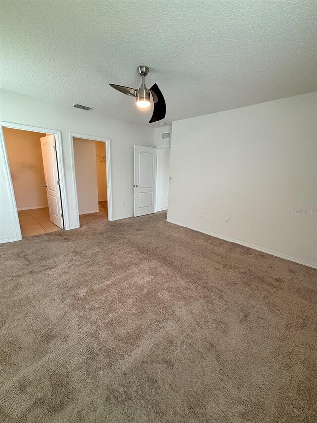 unfurnished bedroom featuring carpet, a spacious closet, visible vents, a closet, and a textured ceiling