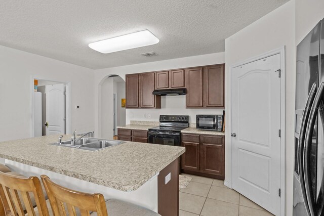 kitchen featuring a sink, visible vents, a breakfast bar, under cabinet range hood, and black appliances