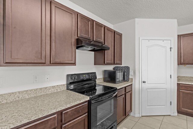 kitchen featuring light countertops, light tile patterned floors, under cabinet range hood, and black appliances