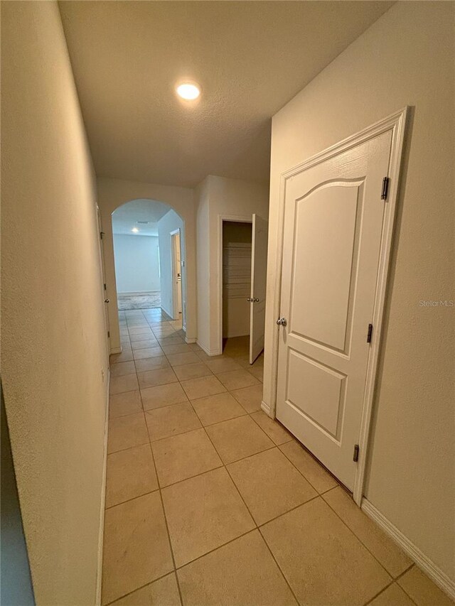 hallway featuring baseboards, arched walkways, recessed lighting, and light tile patterned floors