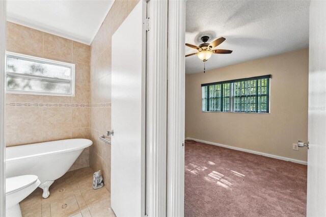 bathroom featuring ceiling fan, toilet, tile patterned flooring, tile walls, and a tub