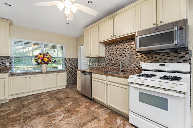 kitchen with appliances with stainless steel finishes, cream cabinets, sink, and backsplash