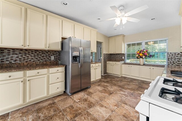 kitchen with backsplash, white range oven, ceiling fan, cream cabinetry, and stainless steel fridge