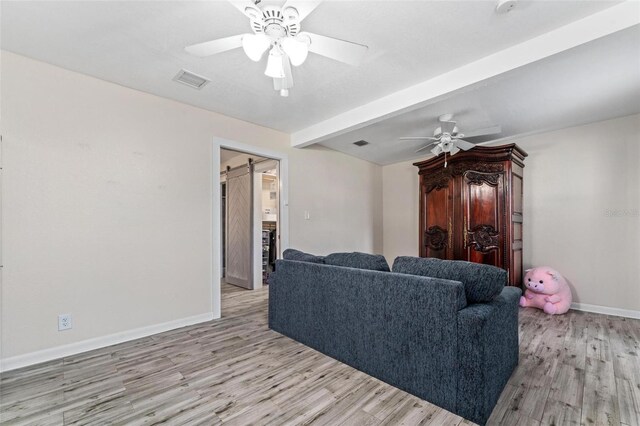 living room with ceiling fan, beam ceiling, a barn door, and light wood-type flooring