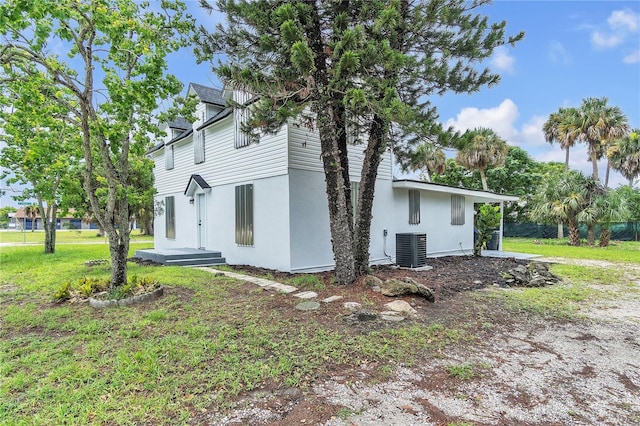 view of side of property featuring central AC unit, a lawn, and stucco siding