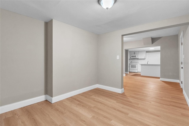 unfurnished dining area with a textured ceiling, light wood finished floors, and baseboards