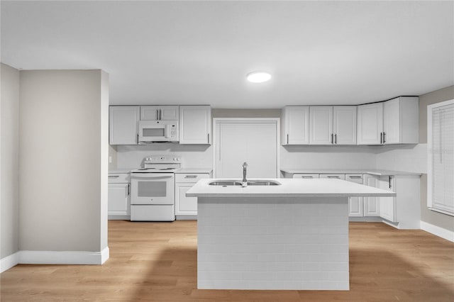 kitchen with white appliances, a center island with sink, light countertops, and a sink