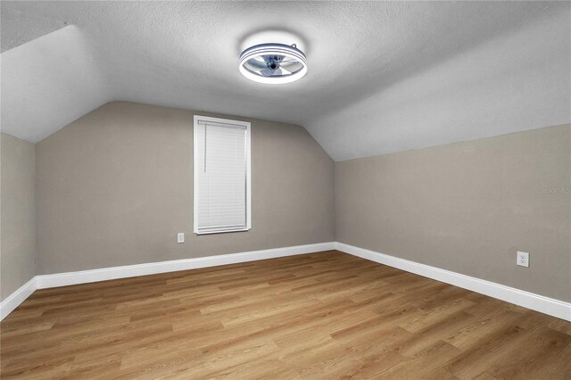 bonus room with a textured ceiling, vaulted ceiling, and light wood-type flooring