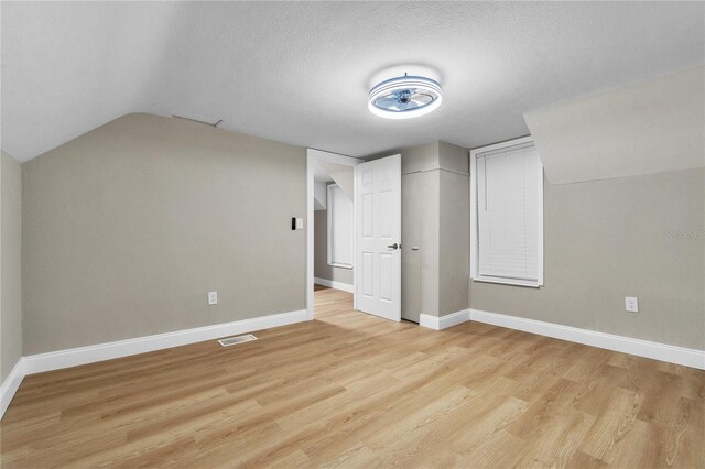 bonus room featuring vaulted ceiling, a textured ceiling, and light hardwood / wood-style flooring