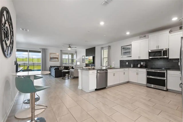 kitchen with ceiling fan, backsplash, white cabinets, kitchen peninsula, and stainless steel appliances