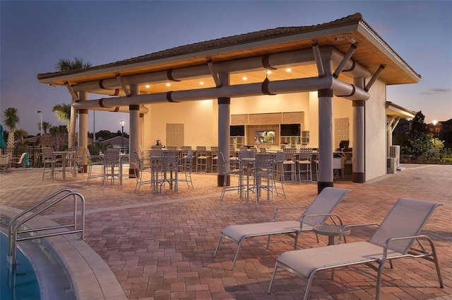 patio terrace at dusk featuring a swimming pool and an outdoor bar