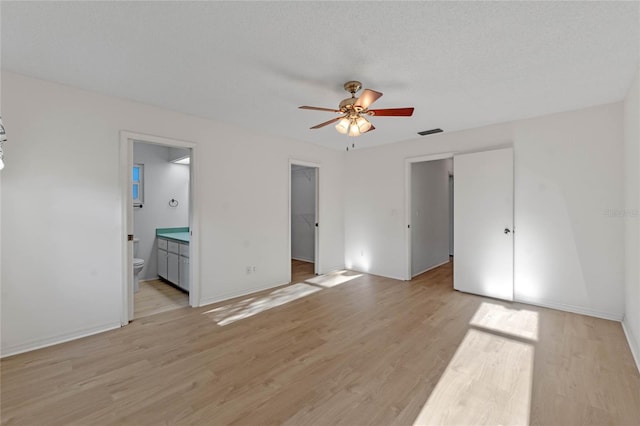 unfurnished bedroom with ceiling fan, a spacious closet, connected bathroom, light hardwood / wood-style floors, and a closet