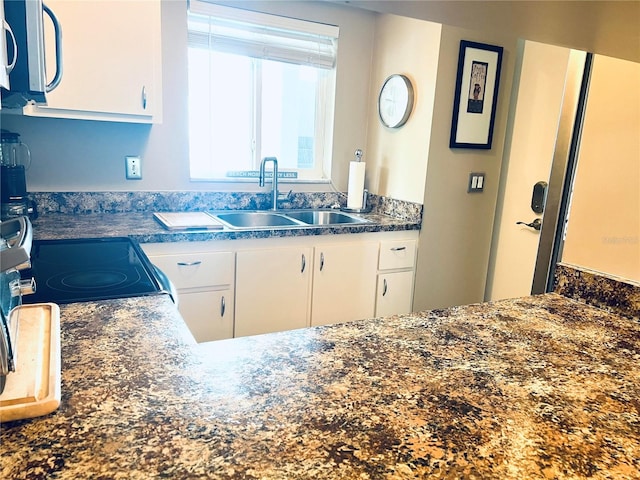 kitchen featuring white cabinets, stove, and sink