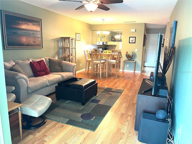 living room with hardwood / wood-style flooring, ceiling fan with notable chandelier, and a textured ceiling