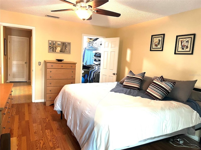 bedroom with a closet, a spacious closet, a textured ceiling, dark wood-type flooring, and ceiling fan