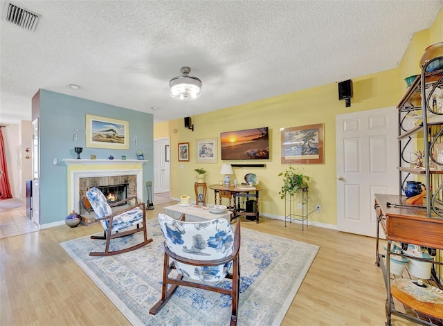 living area with visible vents, baseboards, light wood-style flooring, a glass covered fireplace, and a textured ceiling