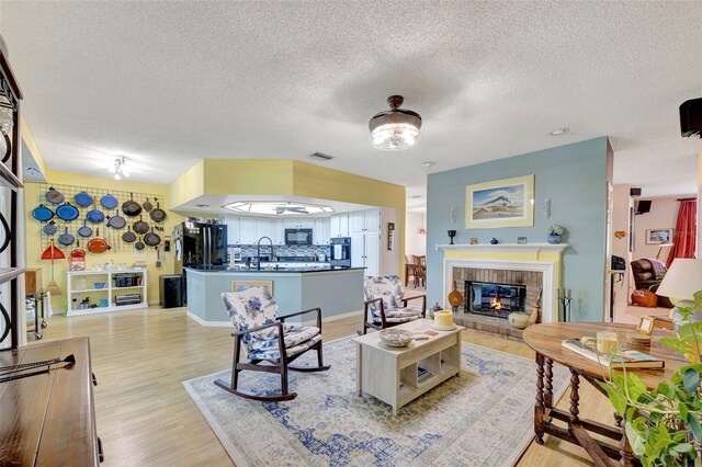 living room featuring light wood-type flooring, sink, a textured ceiling, and a brick fireplace