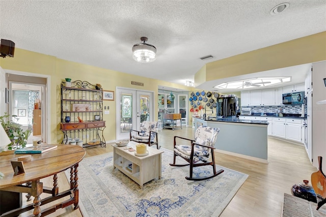 living room featuring french doors, a textured ceiling, light hardwood / wood-style flooring, and a skylight