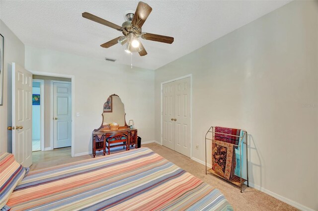 bedroom with a textured ceiling, a closet, ceiling fan, and light carpet